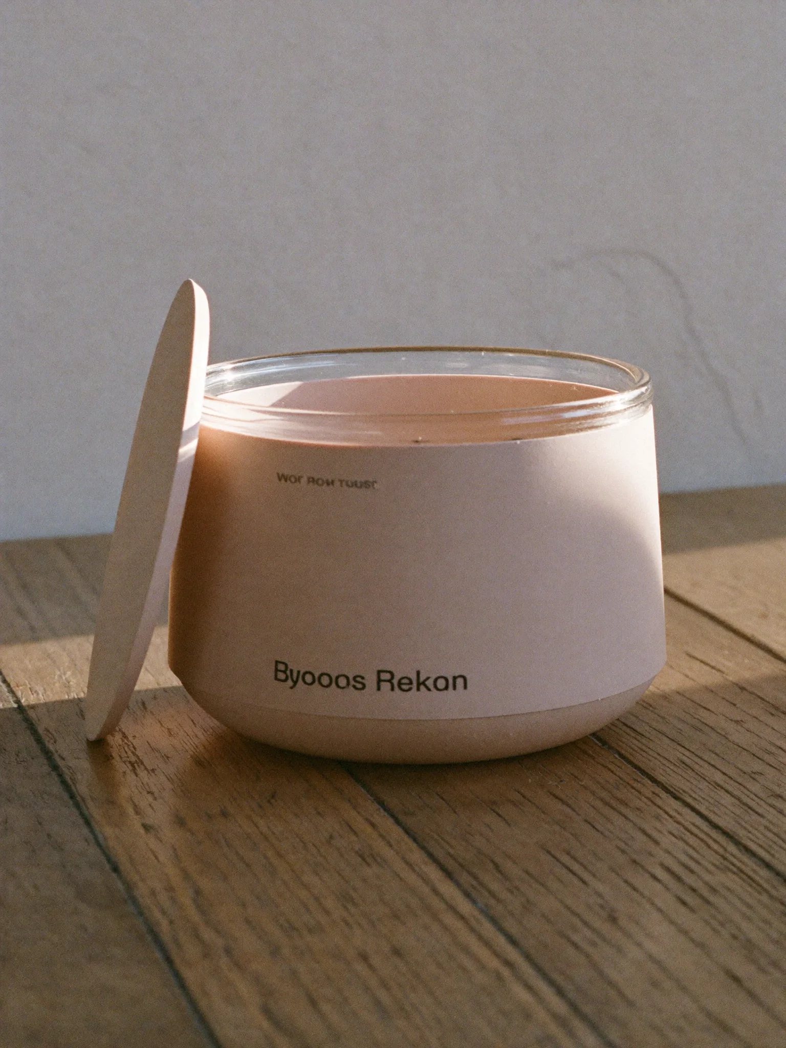 A small glass pot of clay-coloured cream blush with its lid resting against it.