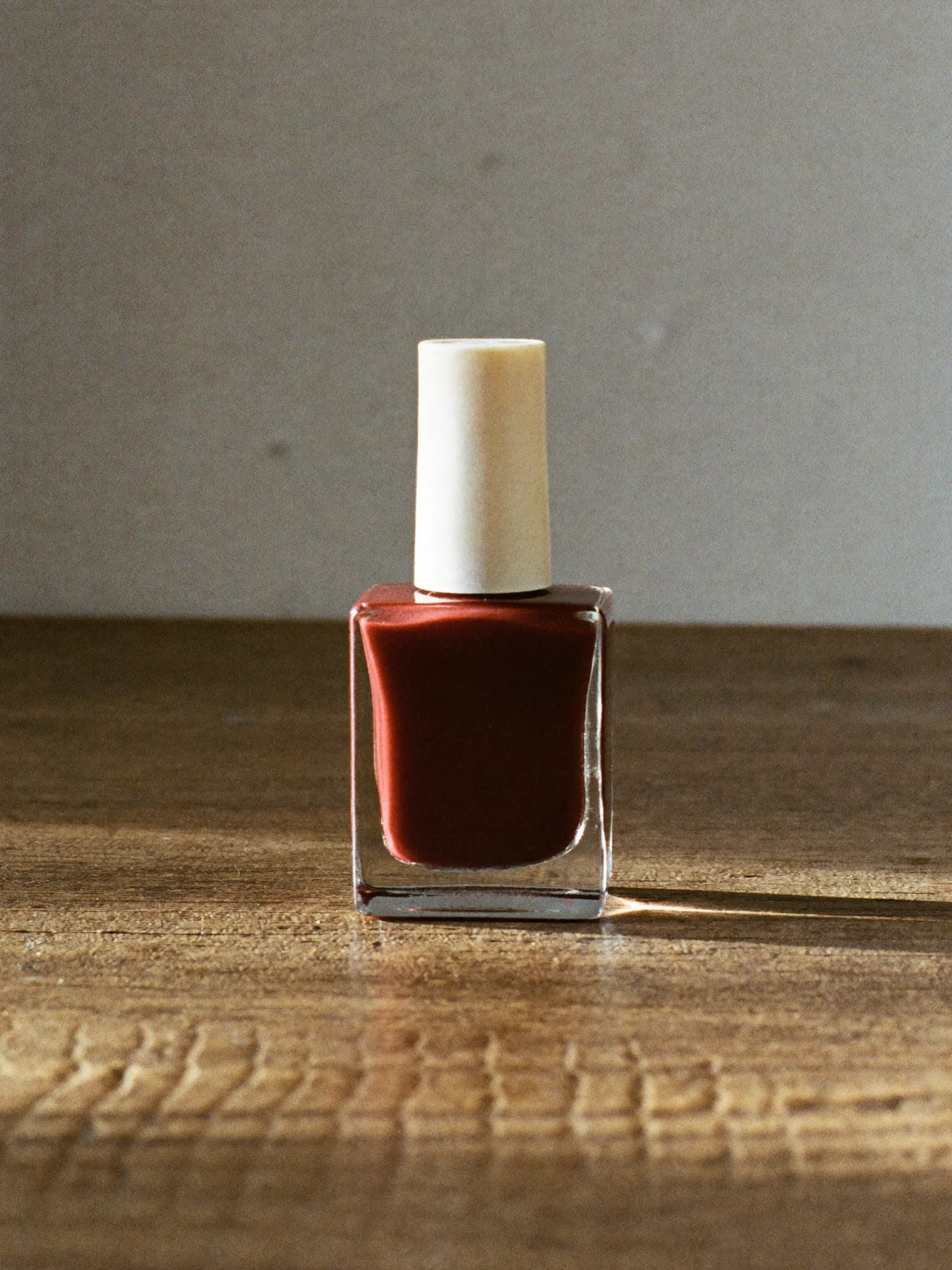 A glass bottle of deep red nail lacquer on a wooden table.